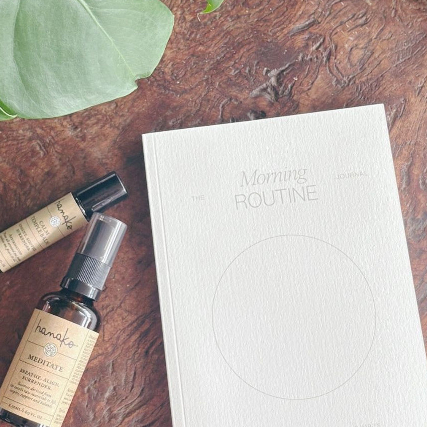 Morning routine journal, meditation spray, calm balm on wooden tray with green plant leaves