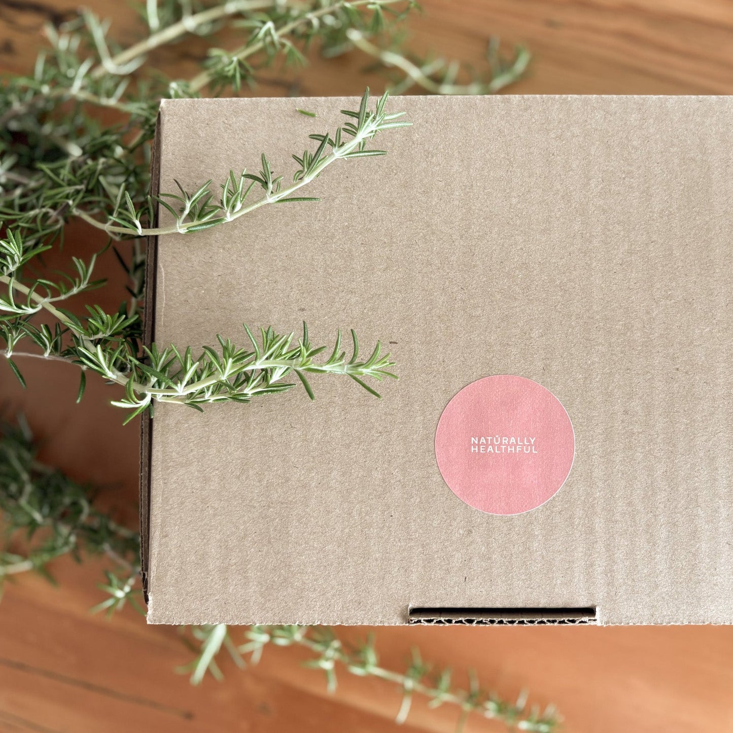 Box with a pink label on a wooden surface with greenery