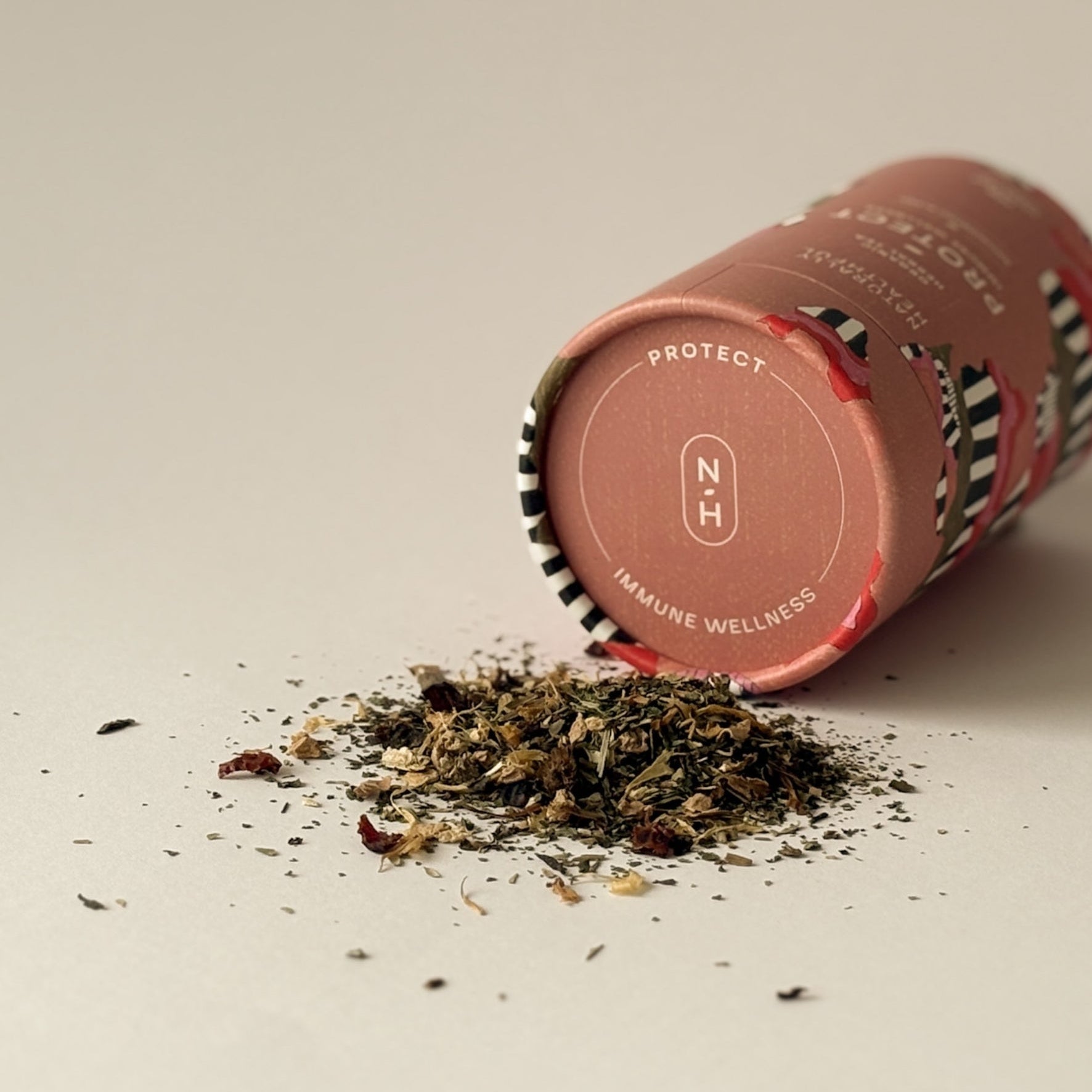 Cylinder of loose leaf immunity tea on it's side with leaves scattered on table