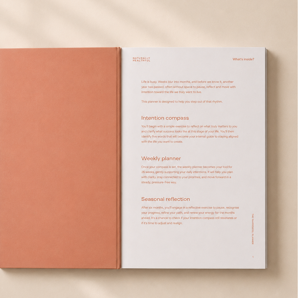 An open planner or journal with a peach-colored cover and white interior pages laid on a warm beige surface with soft diagonal shadows.