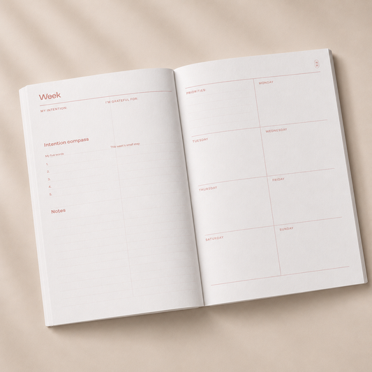 An open weekly planner with blank white pages and light pink printed sections, photographed from above on a warm beige background with soft shadows.