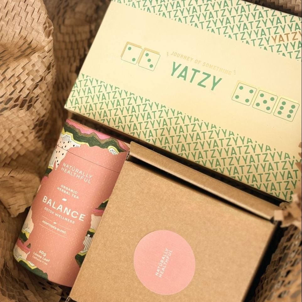 Yatzy game box with a pink bottle labeled 'Balance' on a woven surface